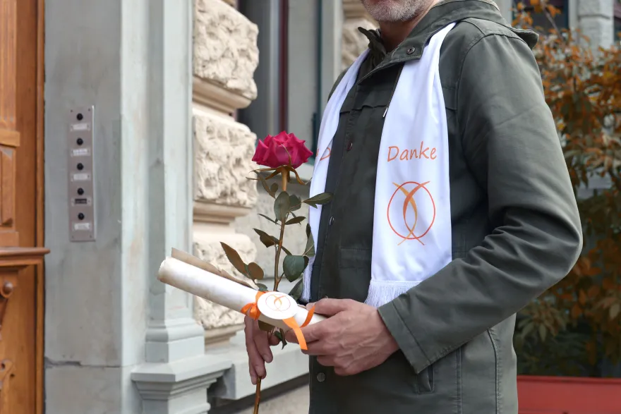 Eine Freiwillige übergibt als Dankeschön einer pflegenden Angehörigen Blumen